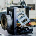 3D printer in operation with a spool of filament on a blurred background