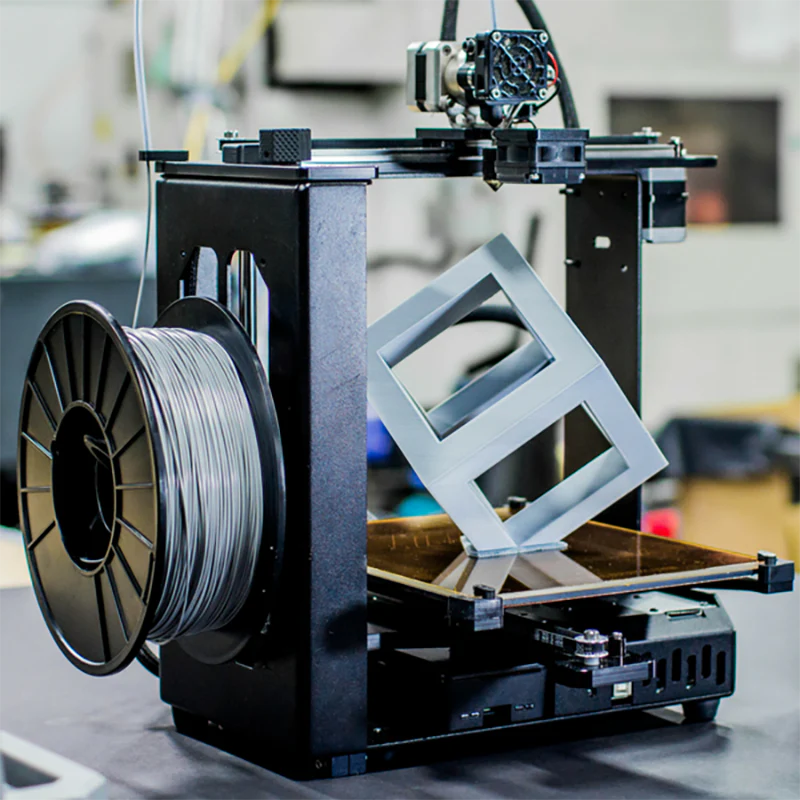 3D printer in operation with a spool of filament on a blurred background