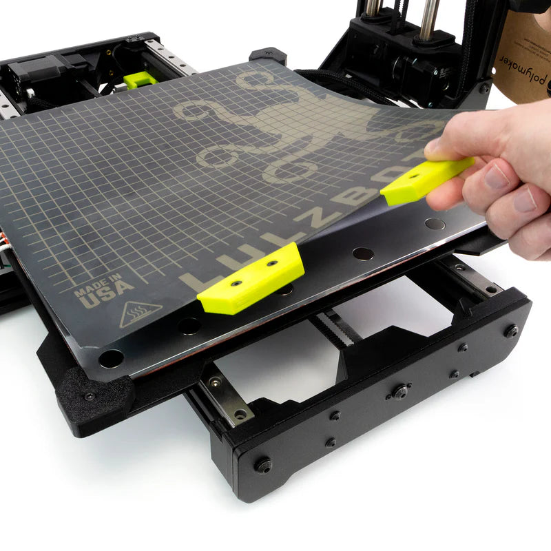 Hand using a yellow grips to adjust a 3D magnetic printer bed.